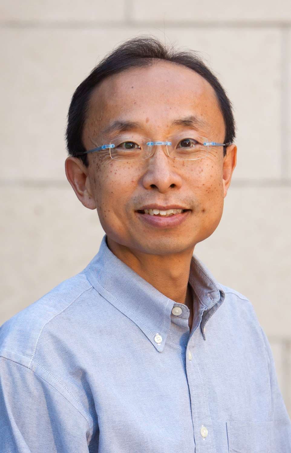 A man with short black hair and glasses smiles warmly.