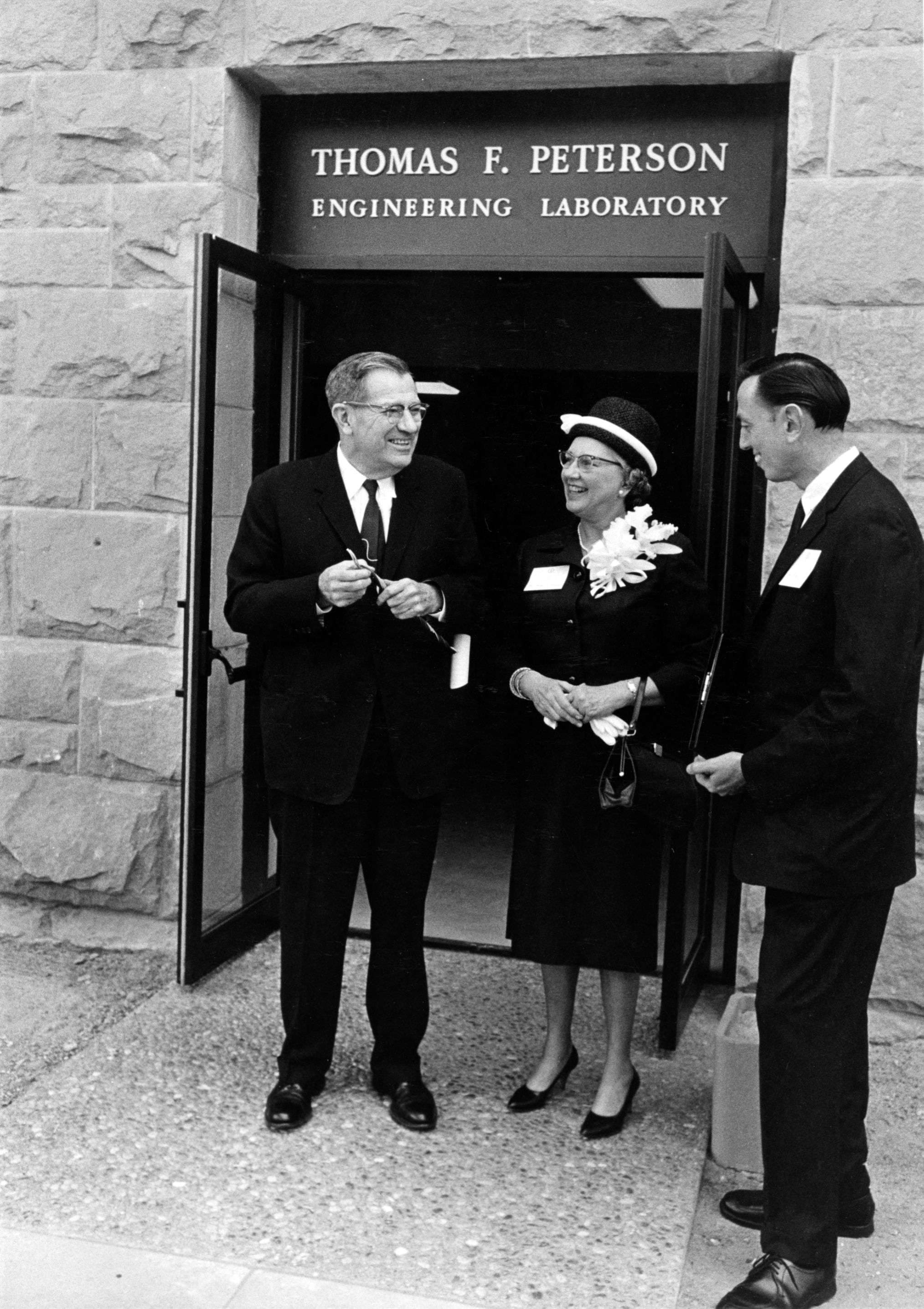 Three individuals, two men and a woman, stand in front of the Thomas F. Peterson Engineering Laboratory building.