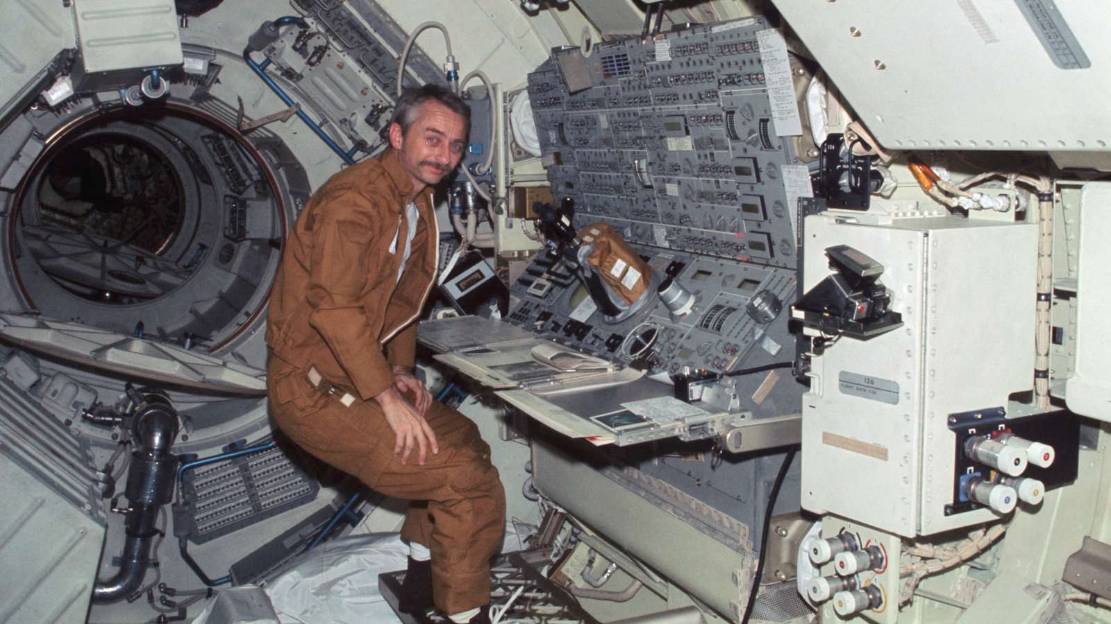 A man wearing an astronaut suit sits in a space station.