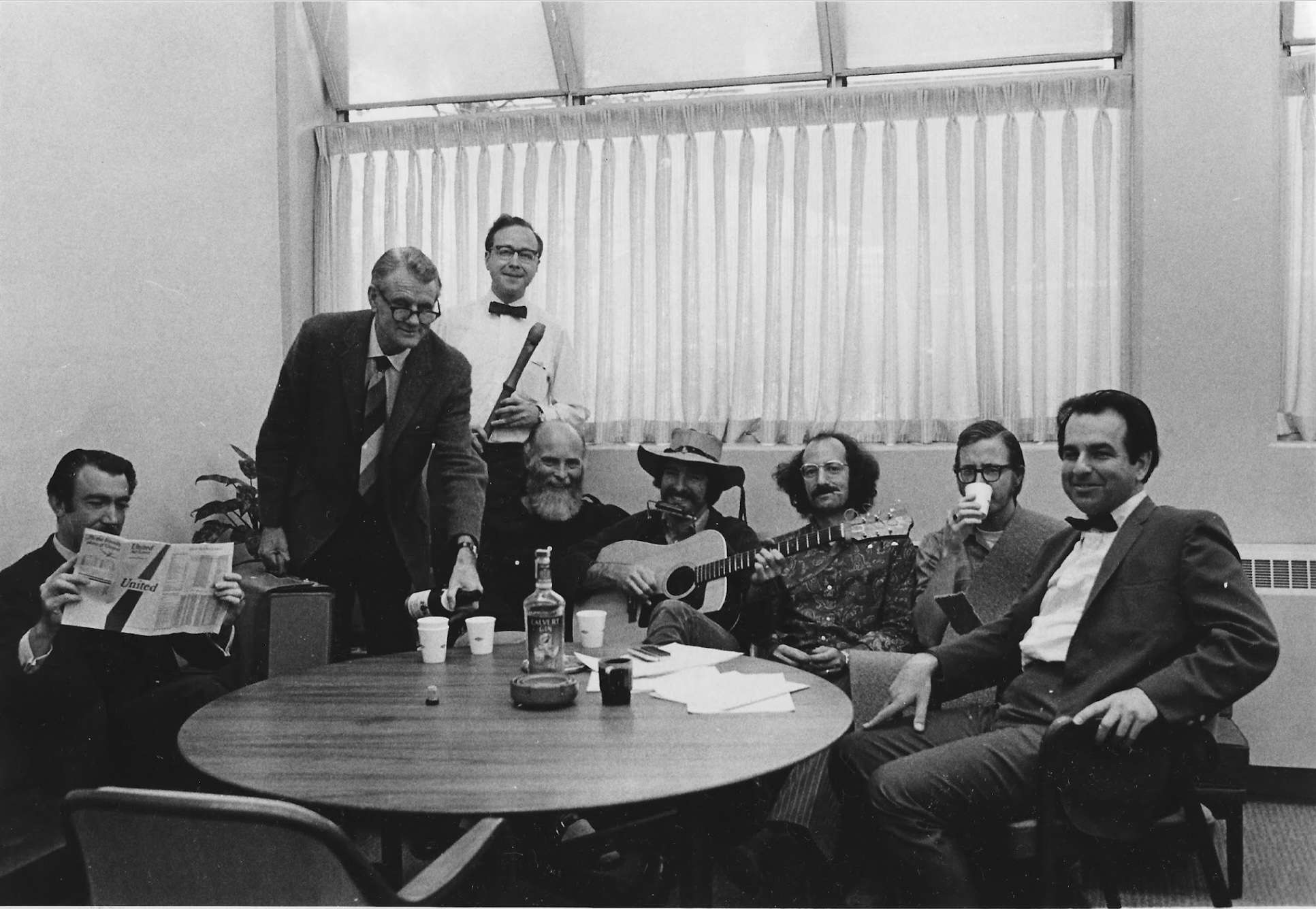Preview of Men gathered at a table playing instruments and drinking a beverage.