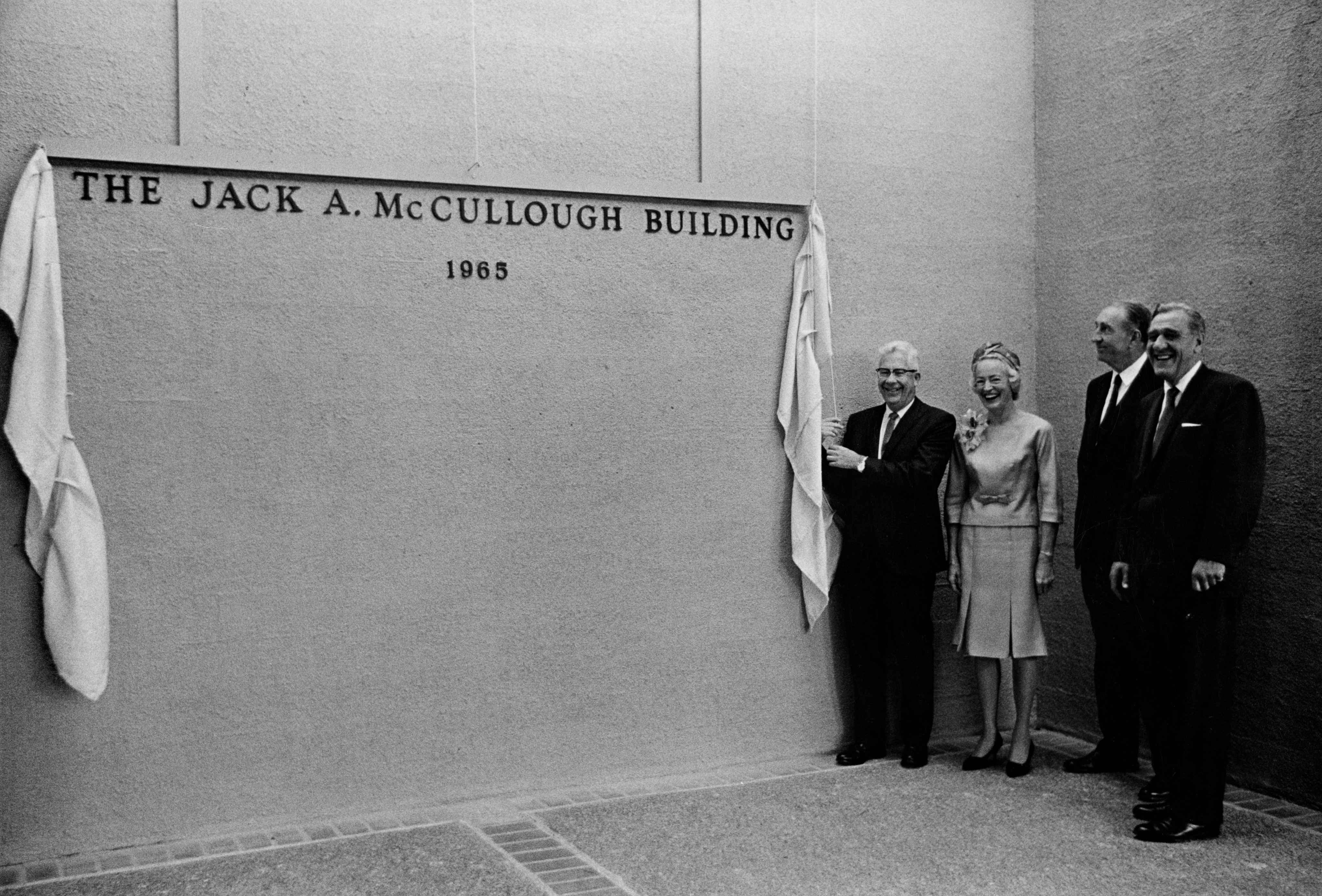 Four individuals, including three men and one woman, reveals the sign for the Jack A. McCullough Building.