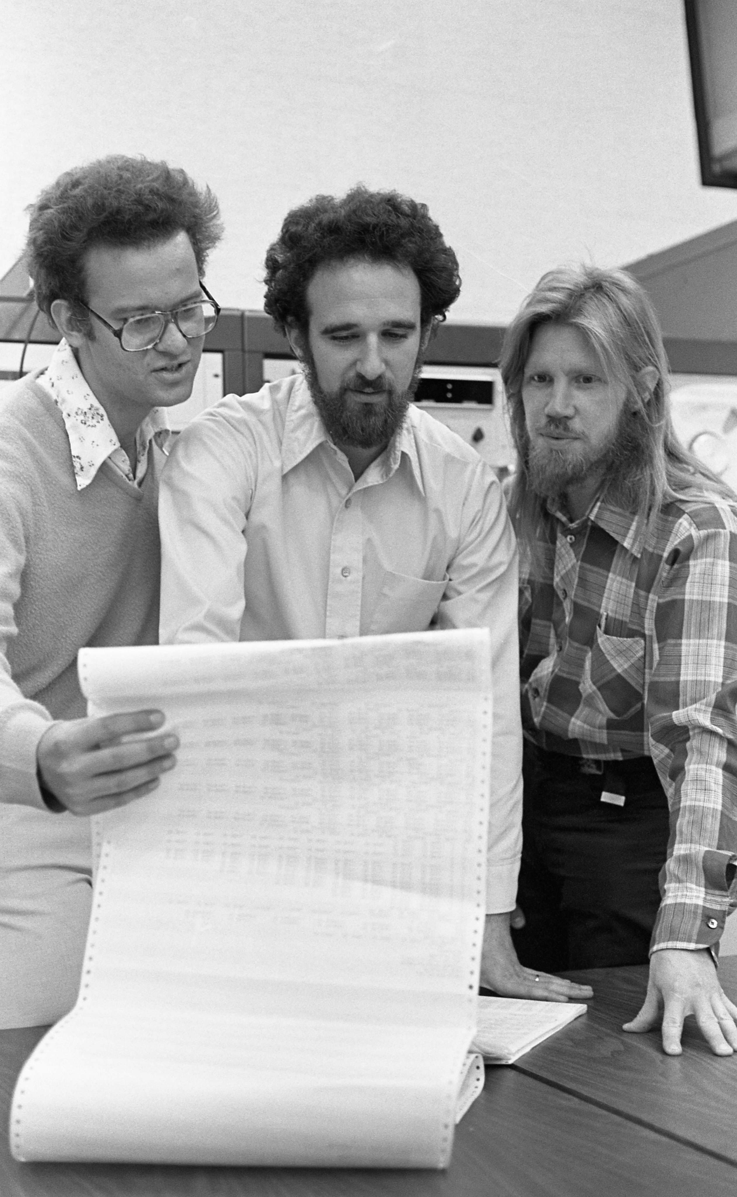 Three men examining a large paper document.