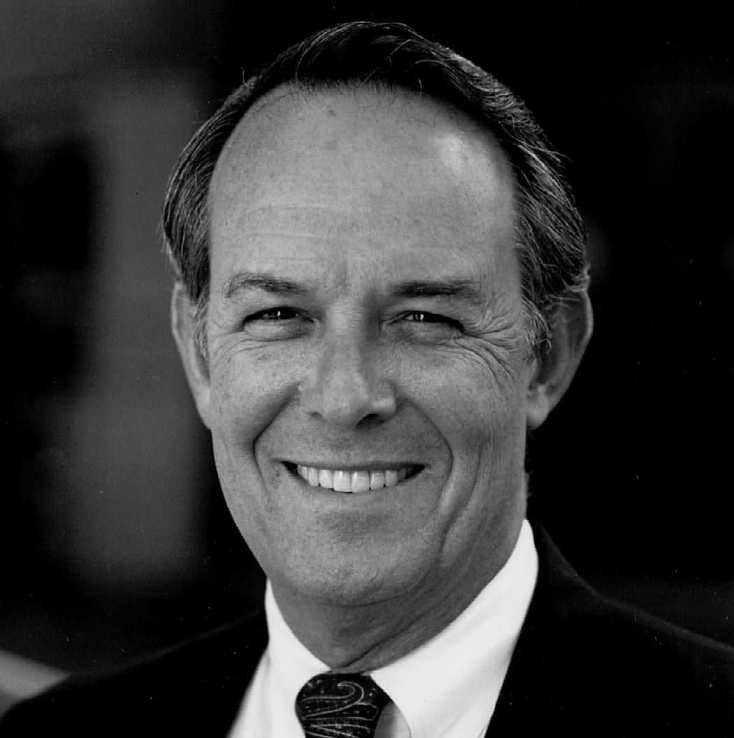 A black and white photo featuring a man dressed in a formal suit and tie.
