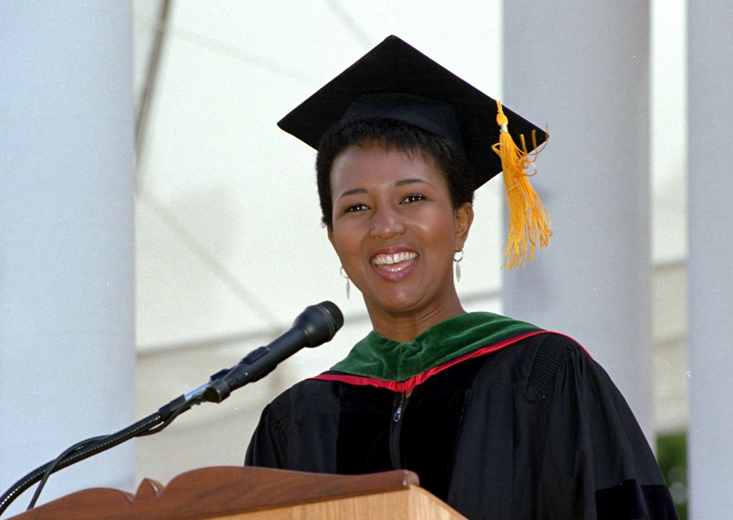 A smiling woman in a graduation gown stands confidently at the podium.