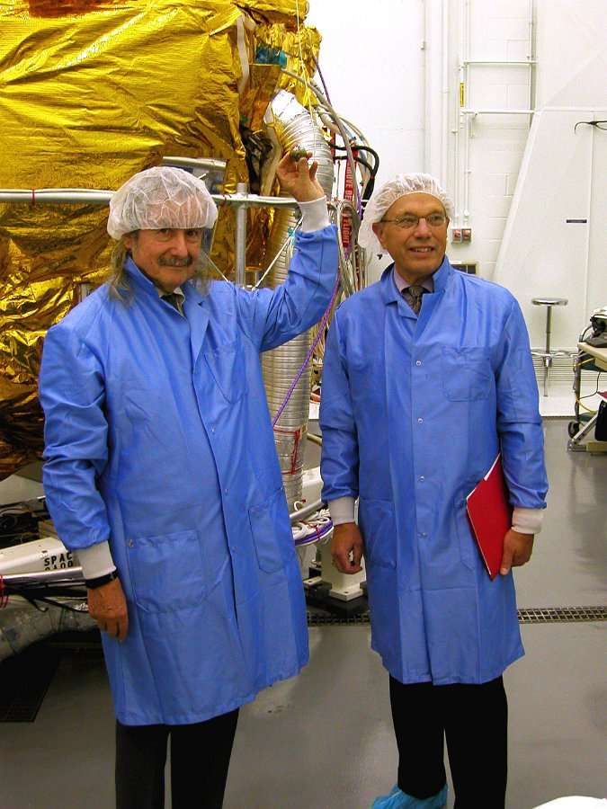 Two men in blue lab coats holding a large an object.