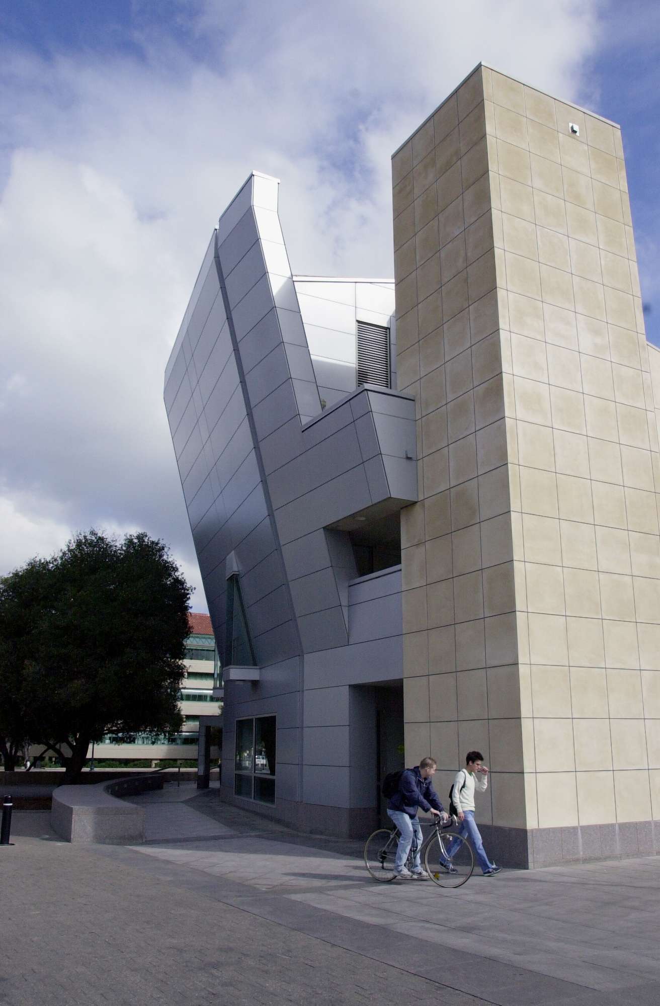A large white building stands prominently beside another structure as two men walk by.