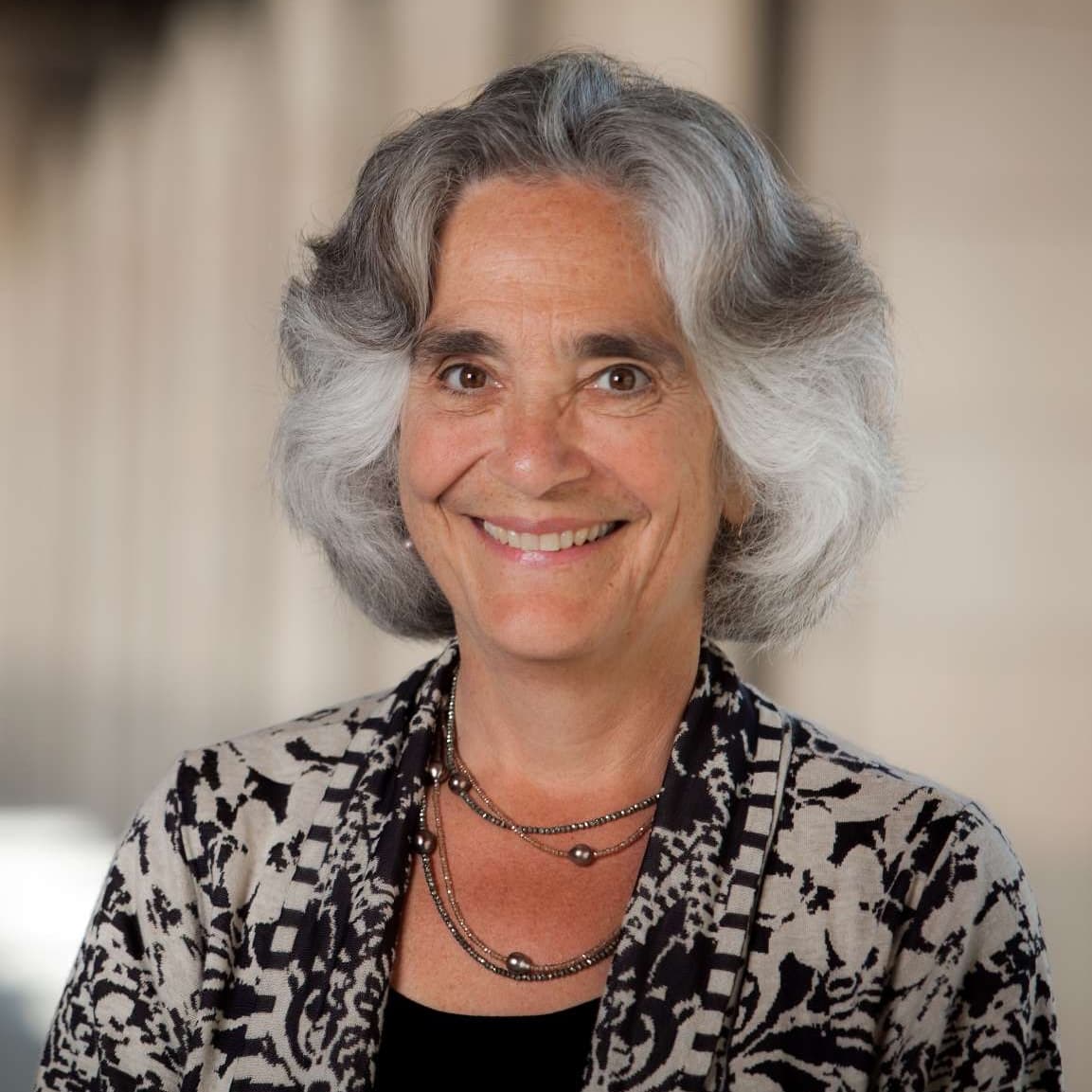 A woman with gray hair wearing a black and white top, smiling softly against a neutral background.