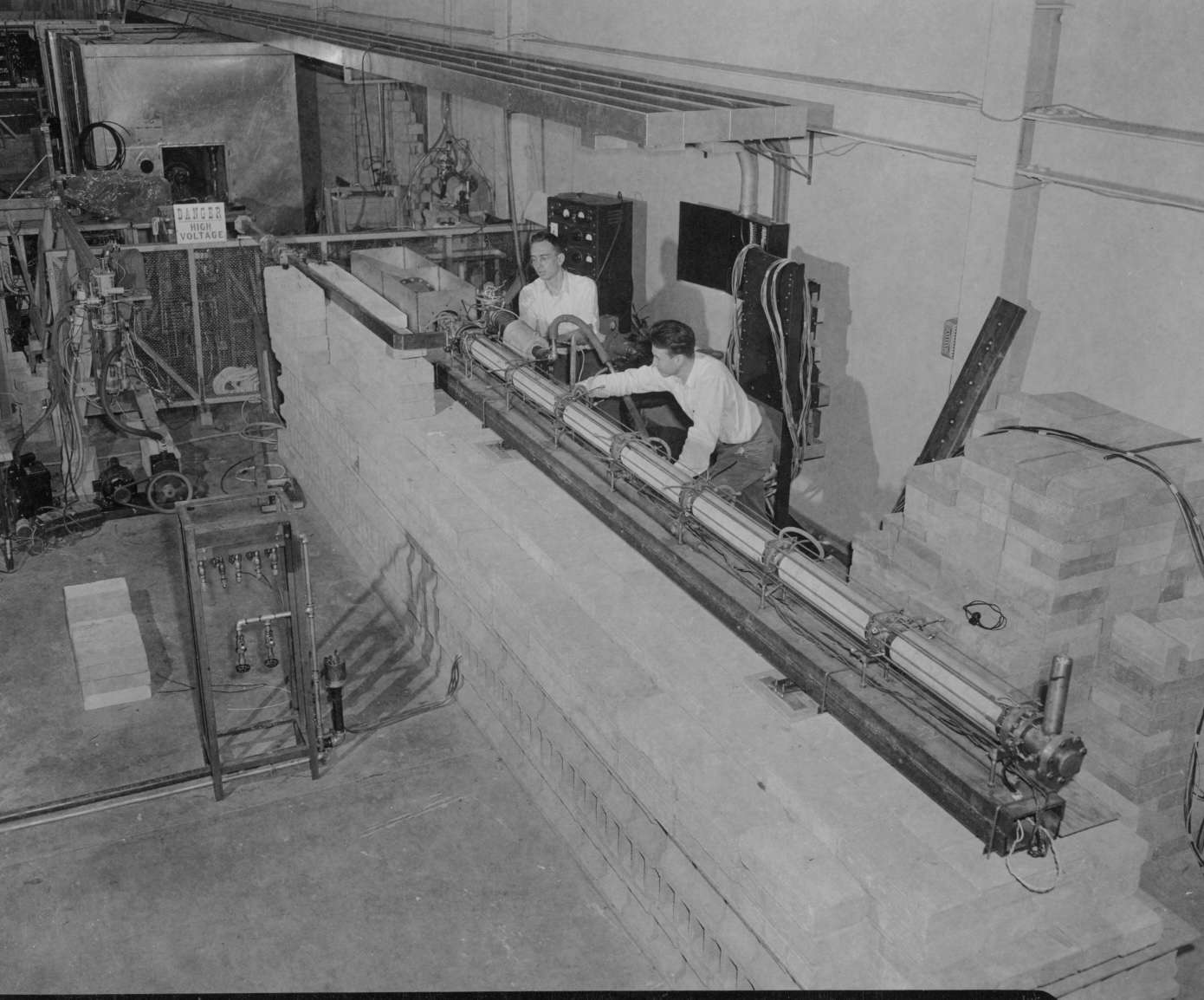 Two men in an indoor room operating on a part of the Mark III linear accelerator