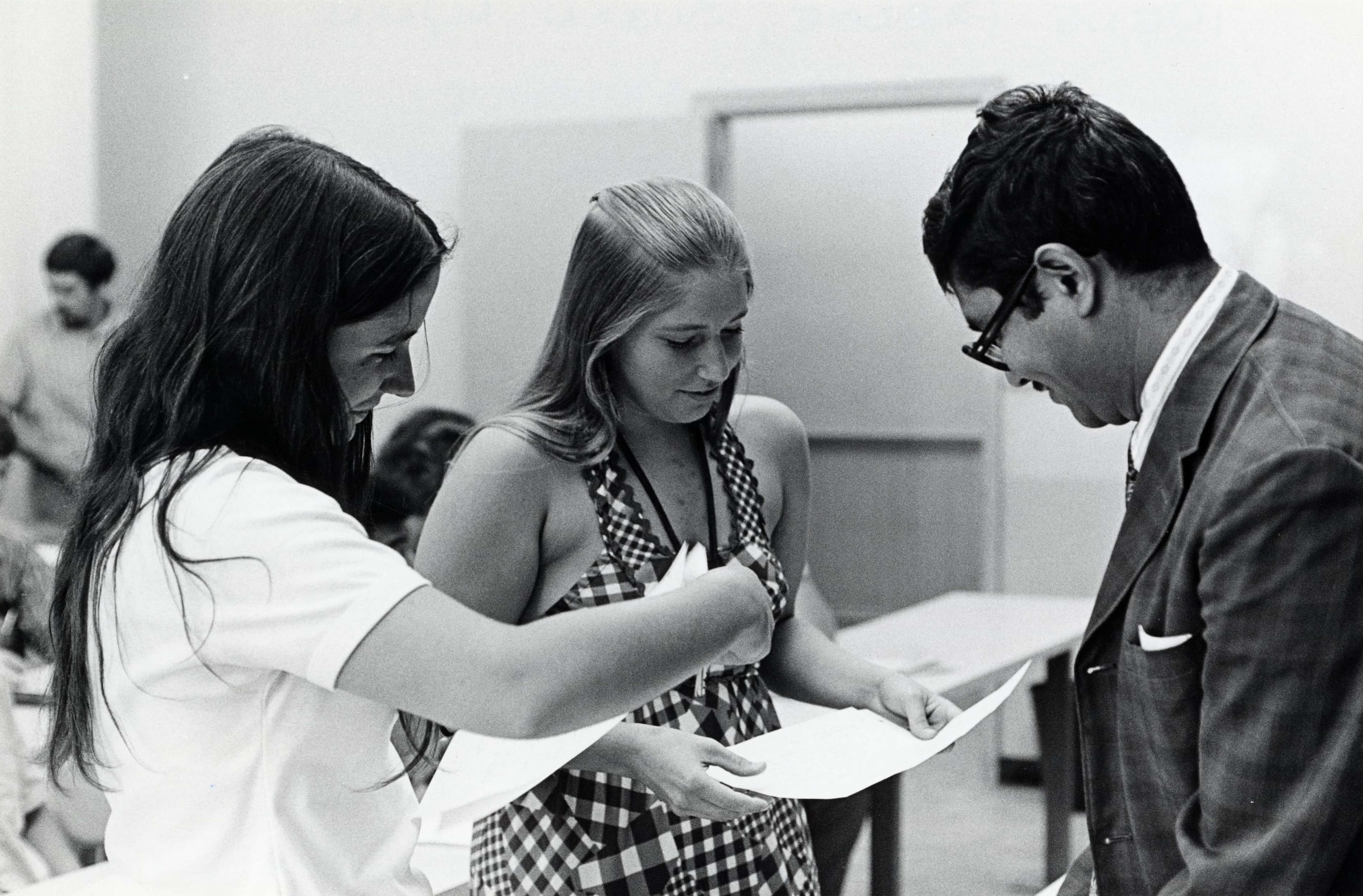 Two woman and a man reviewing documents together in a classroom setting.
