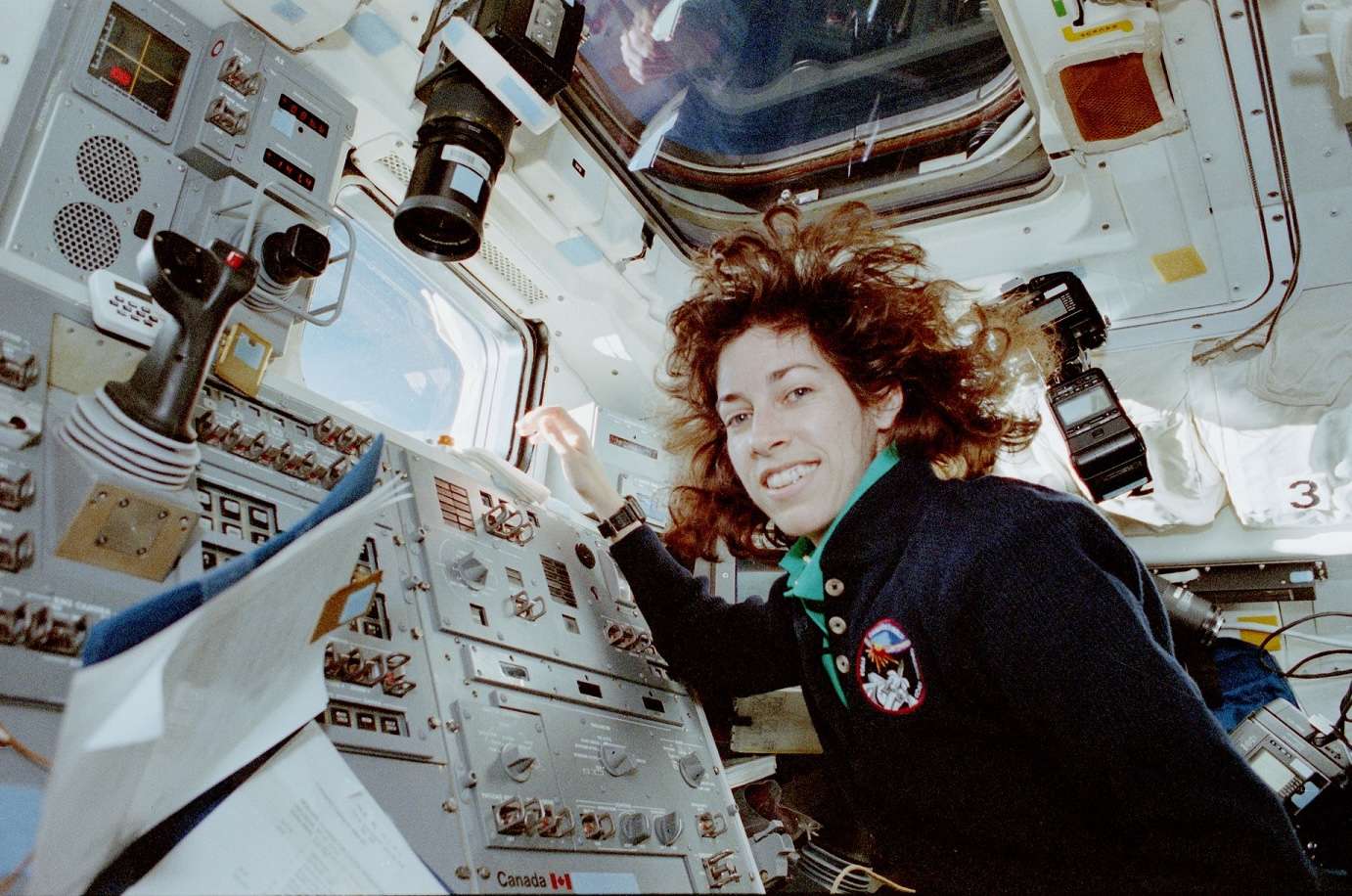A woman wearing a space suit poses before an American flag.