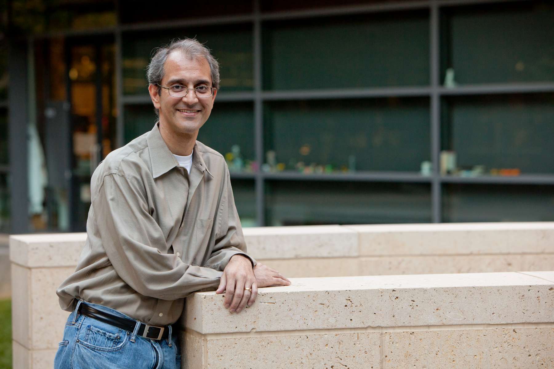 A man in jeans and a shirt leans casually against a wall.