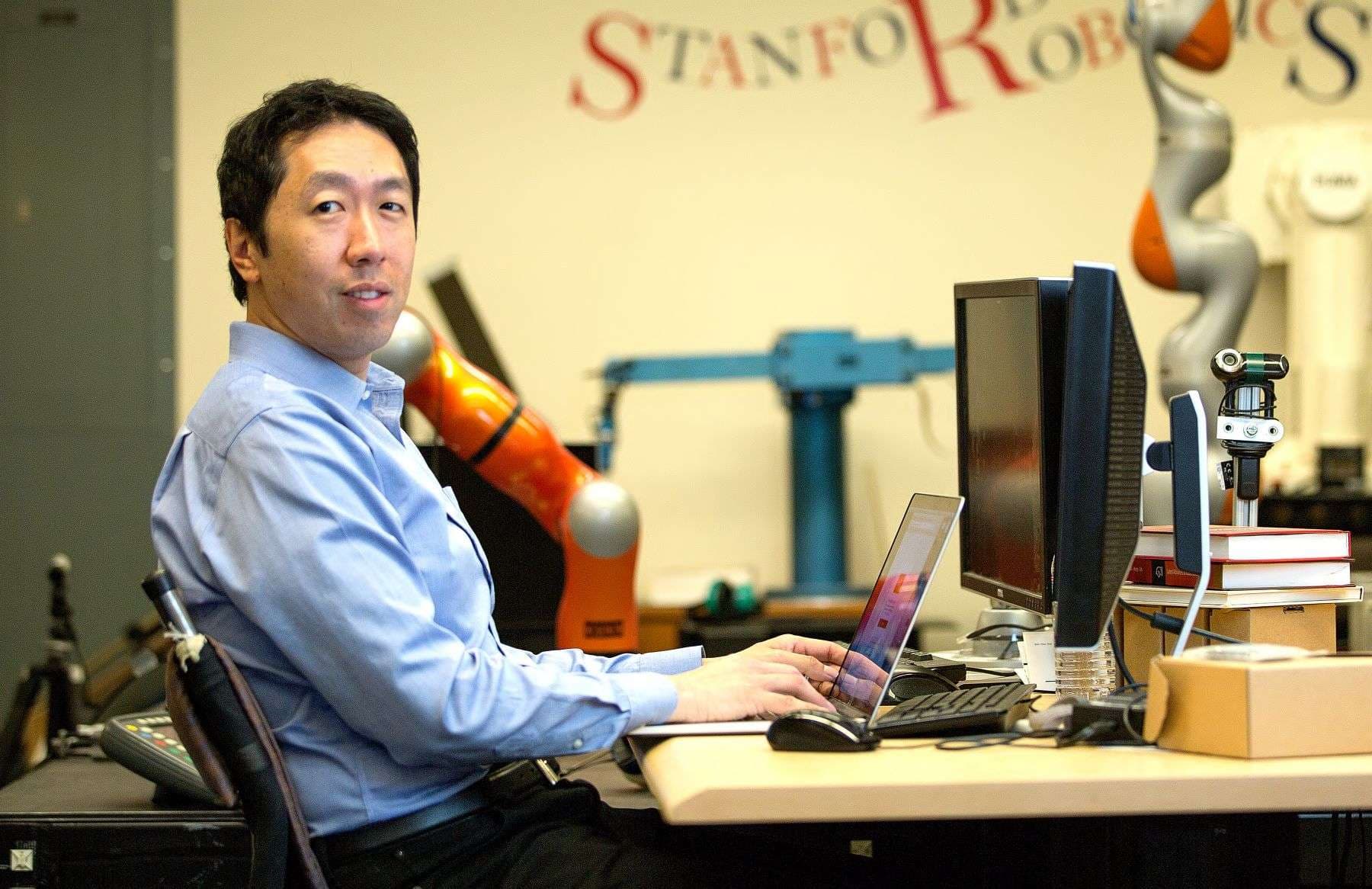 A man in a blue shirt typing on a laptop, seated at a desk with multiple monitors.