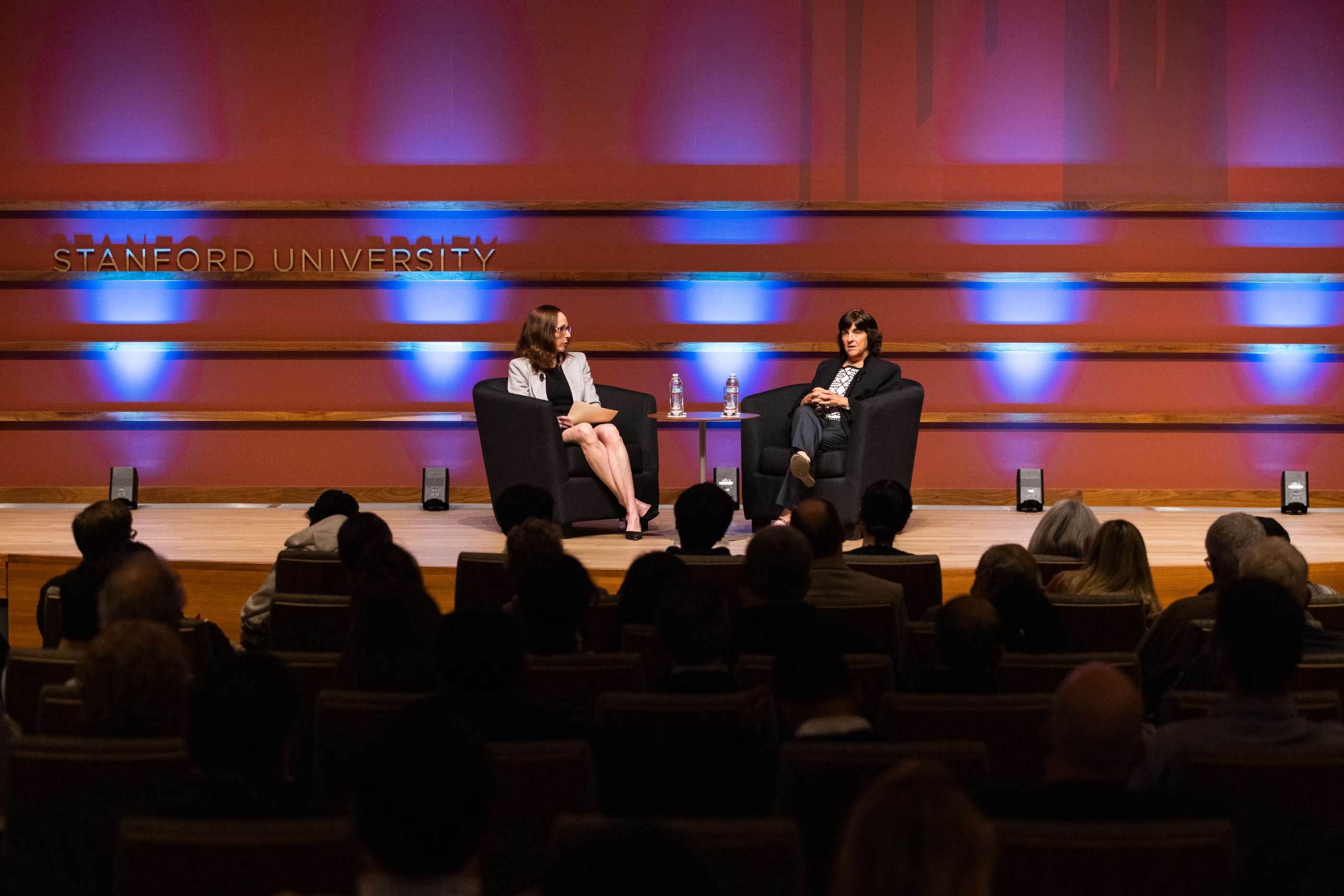 Two women sit in armchairs on stage at a Stanford University event.