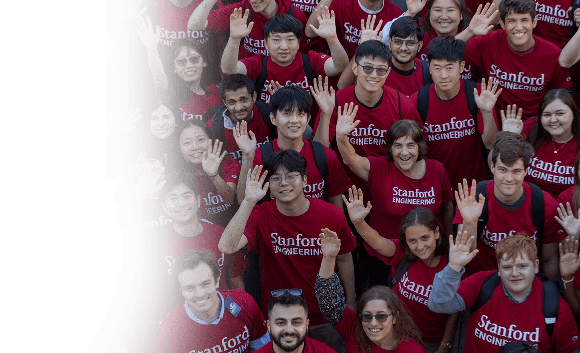 A diverse group of smiling individuals wearing red Stanford Engineering T-shirts wave at the camera.